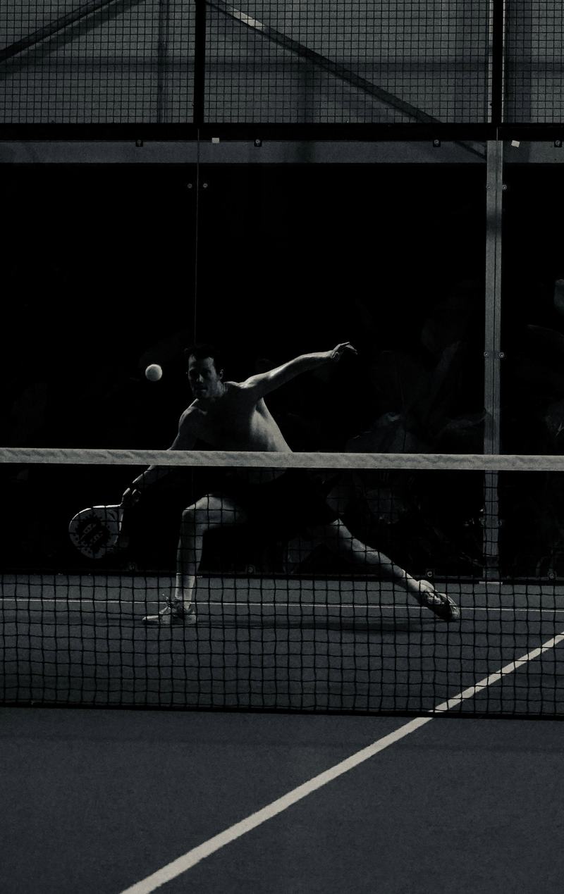 Padel player diving for a low ball on a floodlit court at night