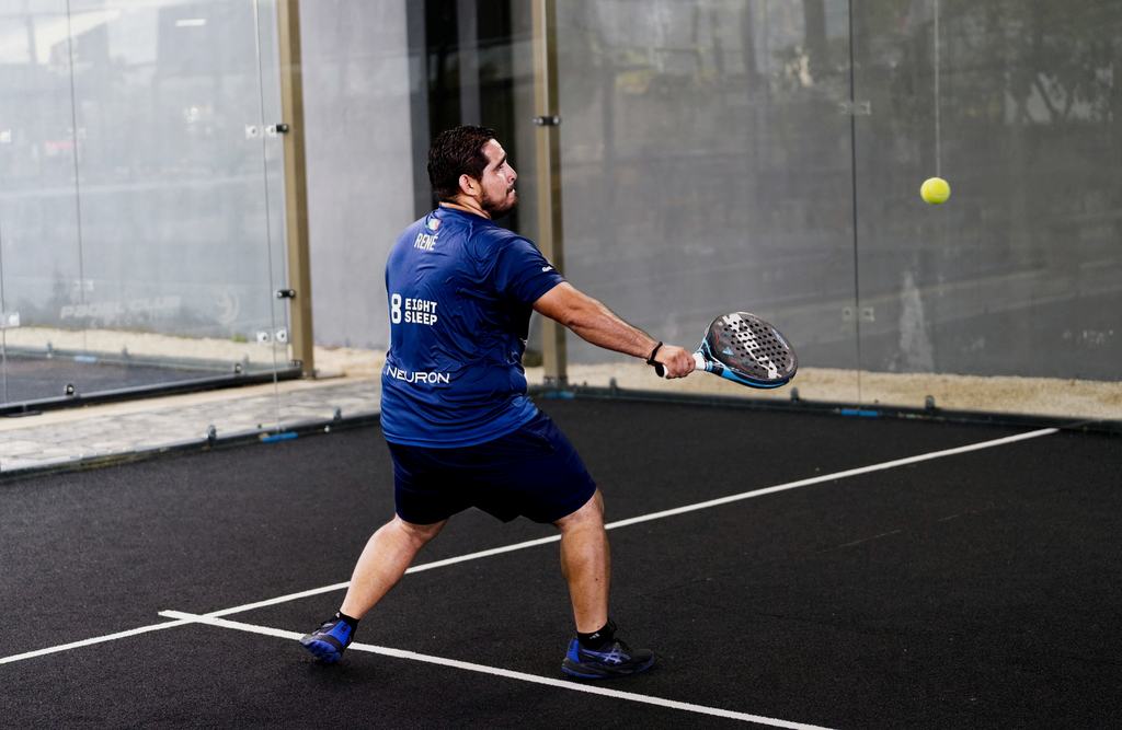Padel player hitting a backhand on an indoor court