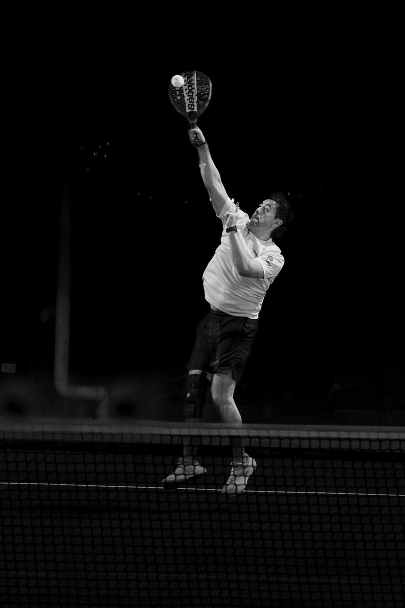 Black and white shot of a padel serve under lights